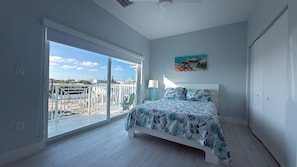 Un dormitorio con cama, un cuadro, una puerta corrediza de vidrio y vista al exterior.