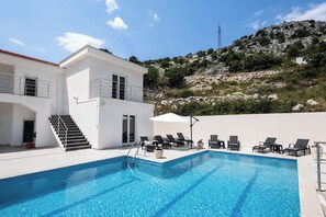 A two-story building with a swimming pool and lounge chairs.