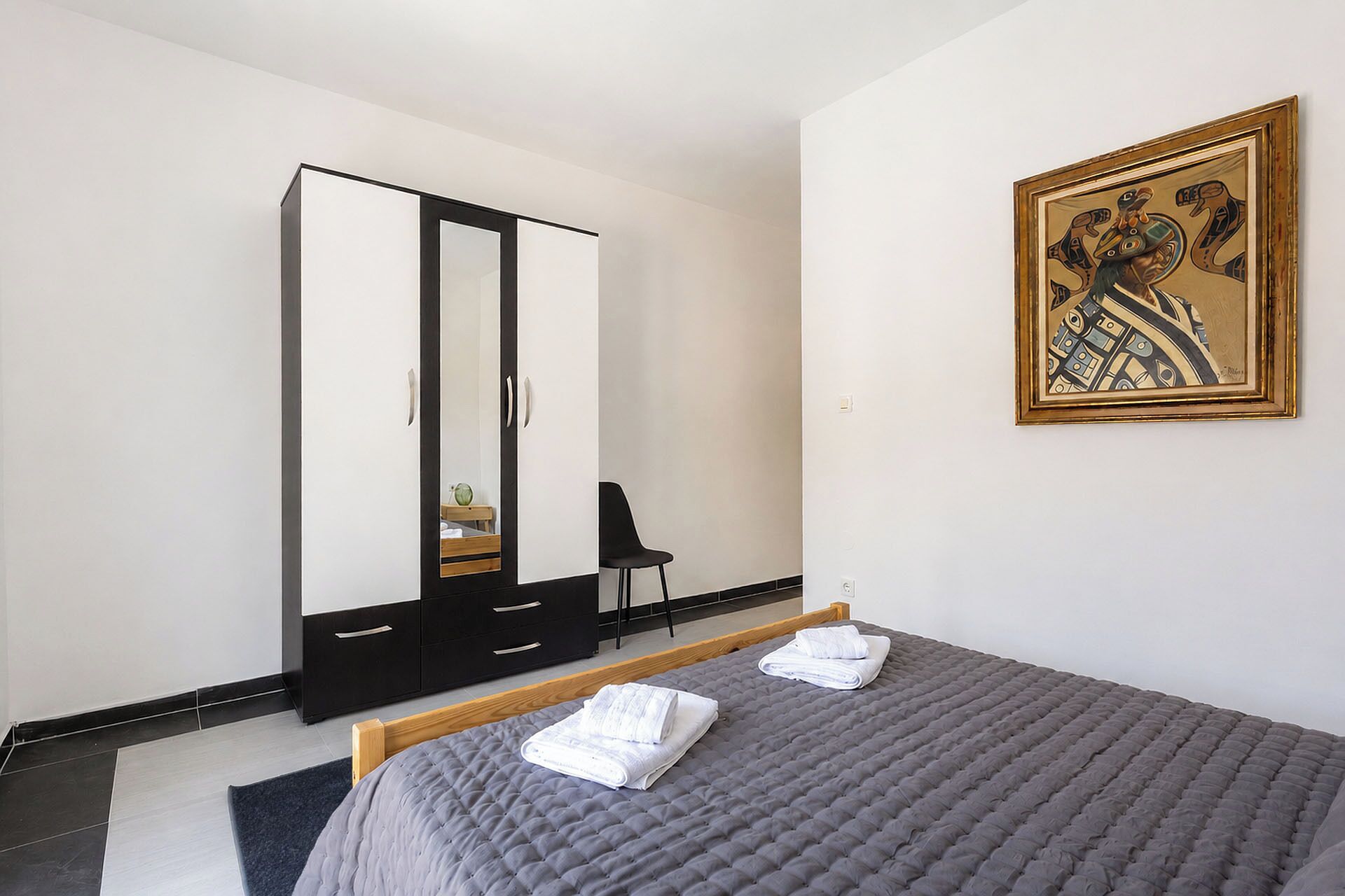 Un dormitorio con cama, armario, silla y un cuadro en la pared.