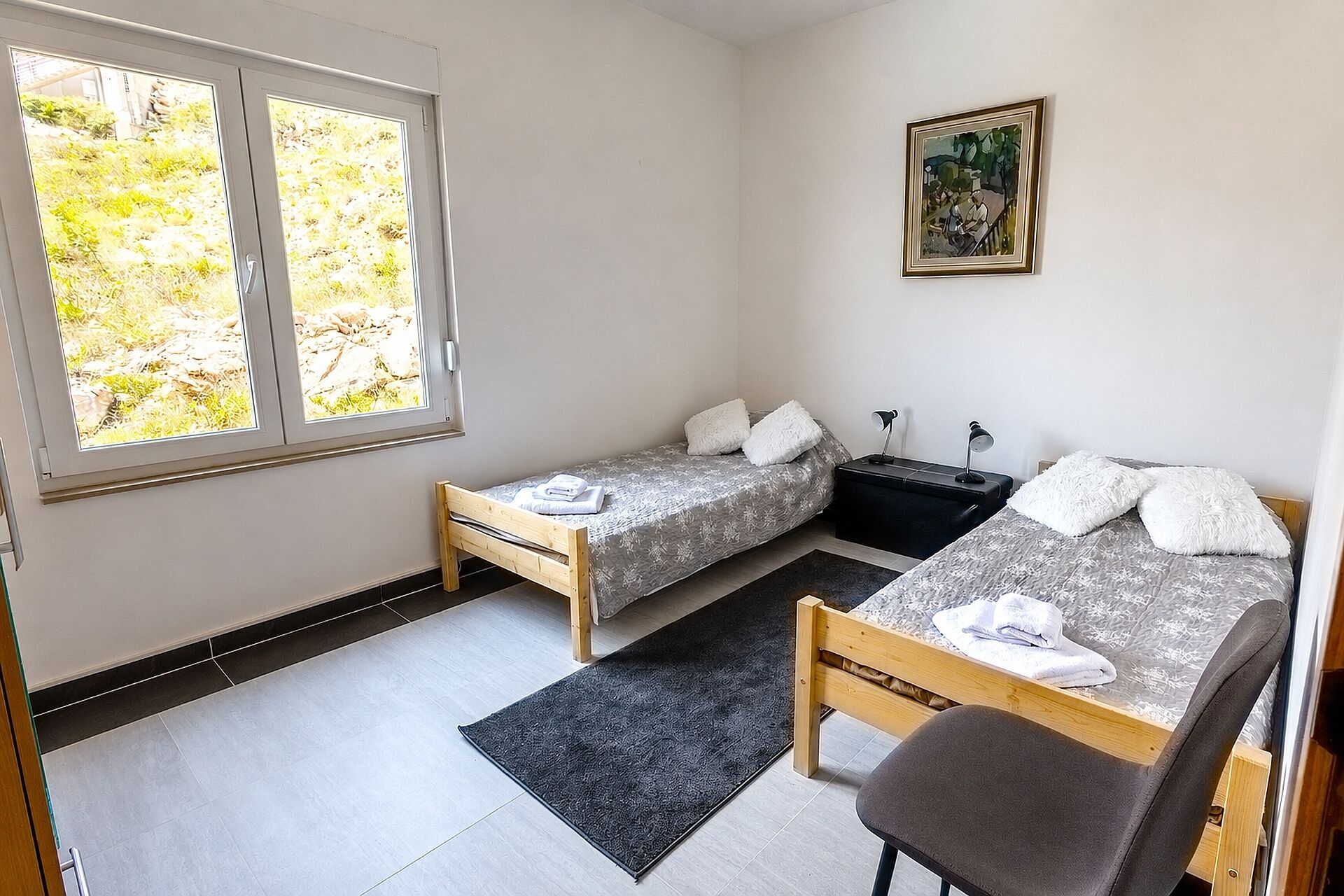 A small, clean room with two beds, a desk, and a chair.