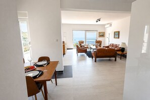 A modern living room with a dining area, large windows, and a view of the outdoors.