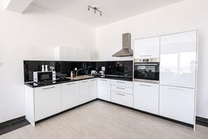 A modern kitchen with white cabinets, black countertops, and stainless steel appliances.