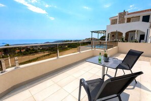 A balcony with a glass table, two chairs, a pool, and a view of the sea.