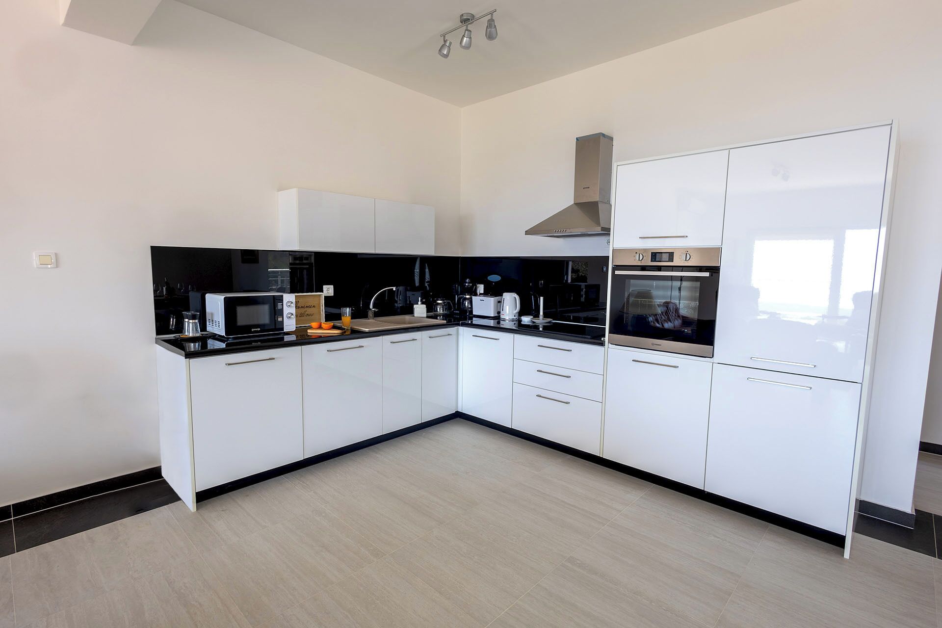 A modern kitchen with white cabinetry, a black countertop, and stainless steel appliances including a microwave, oven, and coffee maker.