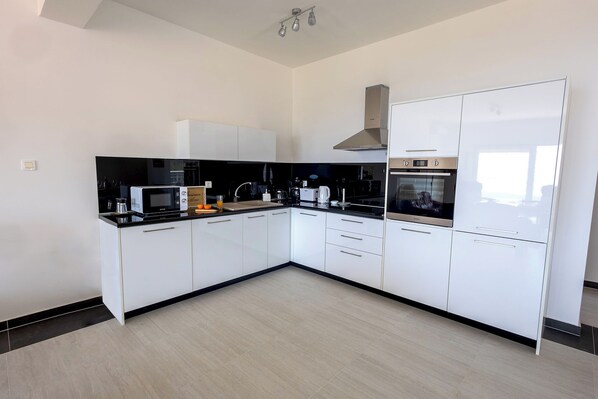 A modern kitchen with white cabinetry, a black countertop, and stainless steel appliances including a microwave, oven, and coffee maker.
