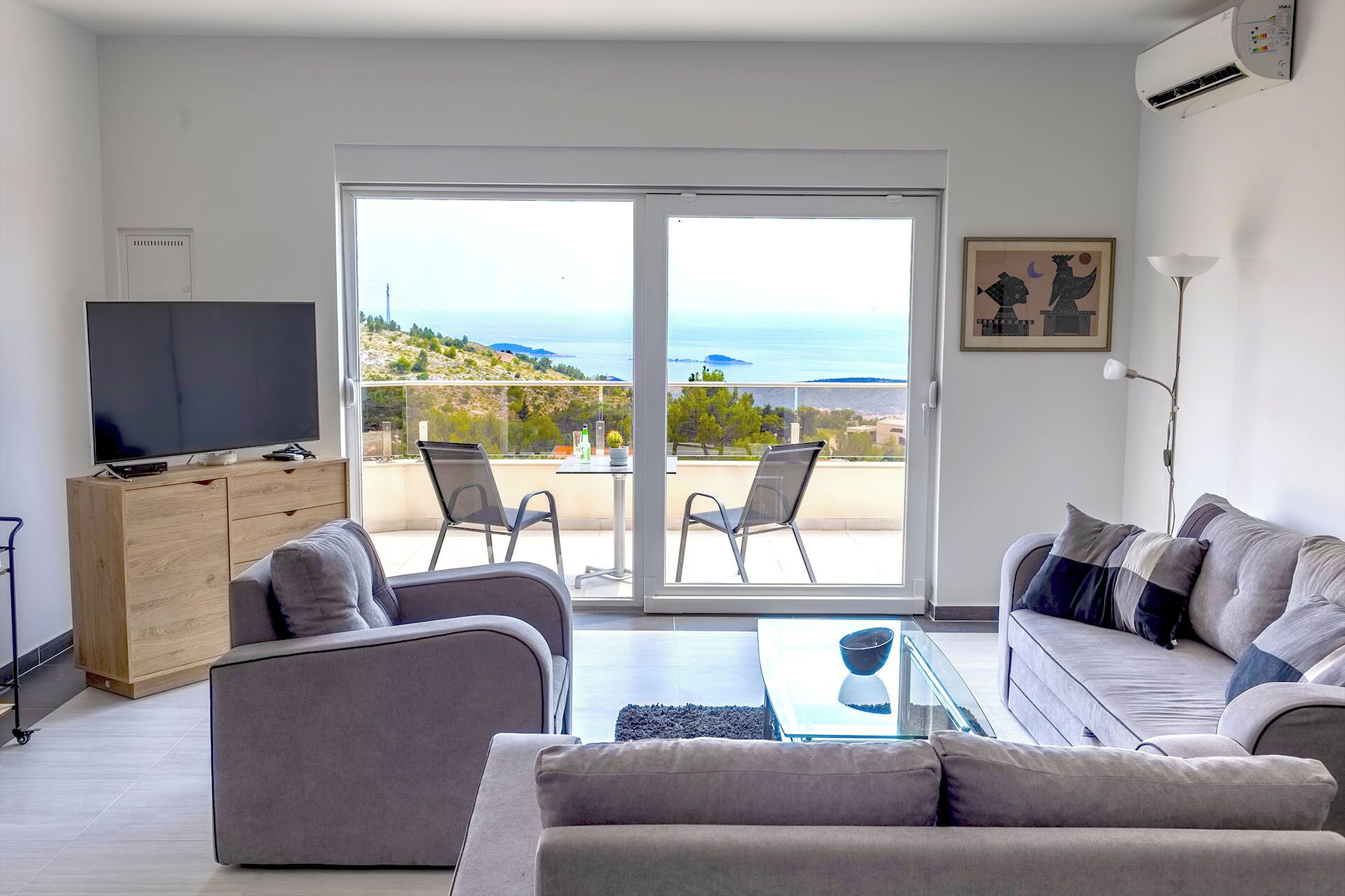 Una sala de estar moderna con un televisor grande, un sofá, una mesa de centro y un balcón con vistas al mar.
