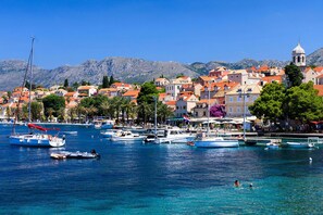 A coastal town with boats docked along the waterfront, a clear blue sea, and buildings with red-tiled roofs.