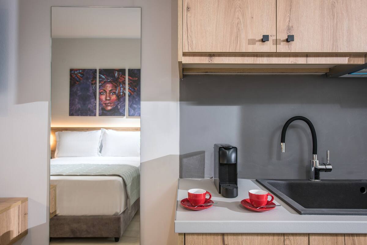Ett modernt hotellrum med en säng, ett litet kök med diskho och en kaffebryggare.