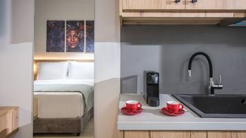 A modern hotel room with a bed, a kitchenette with a sink, and a coffee maker.