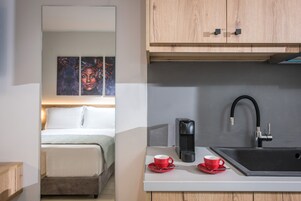 A modern hotel room with a bed, a kitchenette with a sink, and a coffee maker.