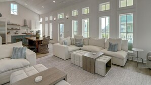 A spacious living room with a large sectional sofa, a coffee table, and a dining area with wicker chairs. - Mod, Designer Beach Home w/ Great On-Site Amenities in Cinnamon Shore (Port Aransas)