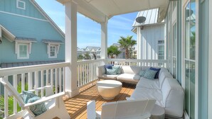 A covered outdoor deck with white railings, a sofa set, and a round table. - Mod, Designer Beach Home w/ Great On-Site Amenities in Cinnamon Shore (Port Aransas)