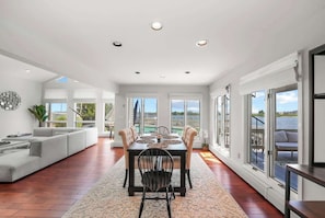 A spacious living room with a dining area, large windows, and a view of the water.
