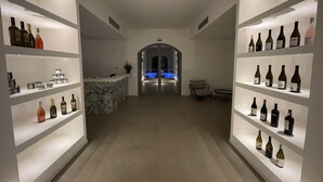 Een hotellobby met een centraal receptiegedeelte, een zwembad op de achtergrond en aan weerszijden rekken met wijnflessen.