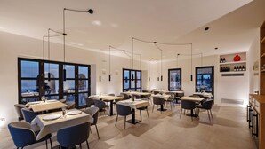 Een moderne eetruimte met meerdere tafels en stoelen, grote ramen en hanglampen.