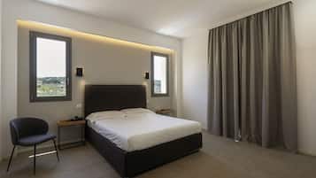 Ein modernes Schlafzimmer mit einem großen Bett, zwei Nachttischen, einem Sessel und Blick ins Freie durch zwei Fenster.