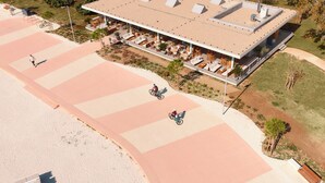 Luftaufnahme eines Strandreisorts mit einer überdachten Außenbereich-Sitzgelegenheit, einem Radweg und einem Sandstrand.