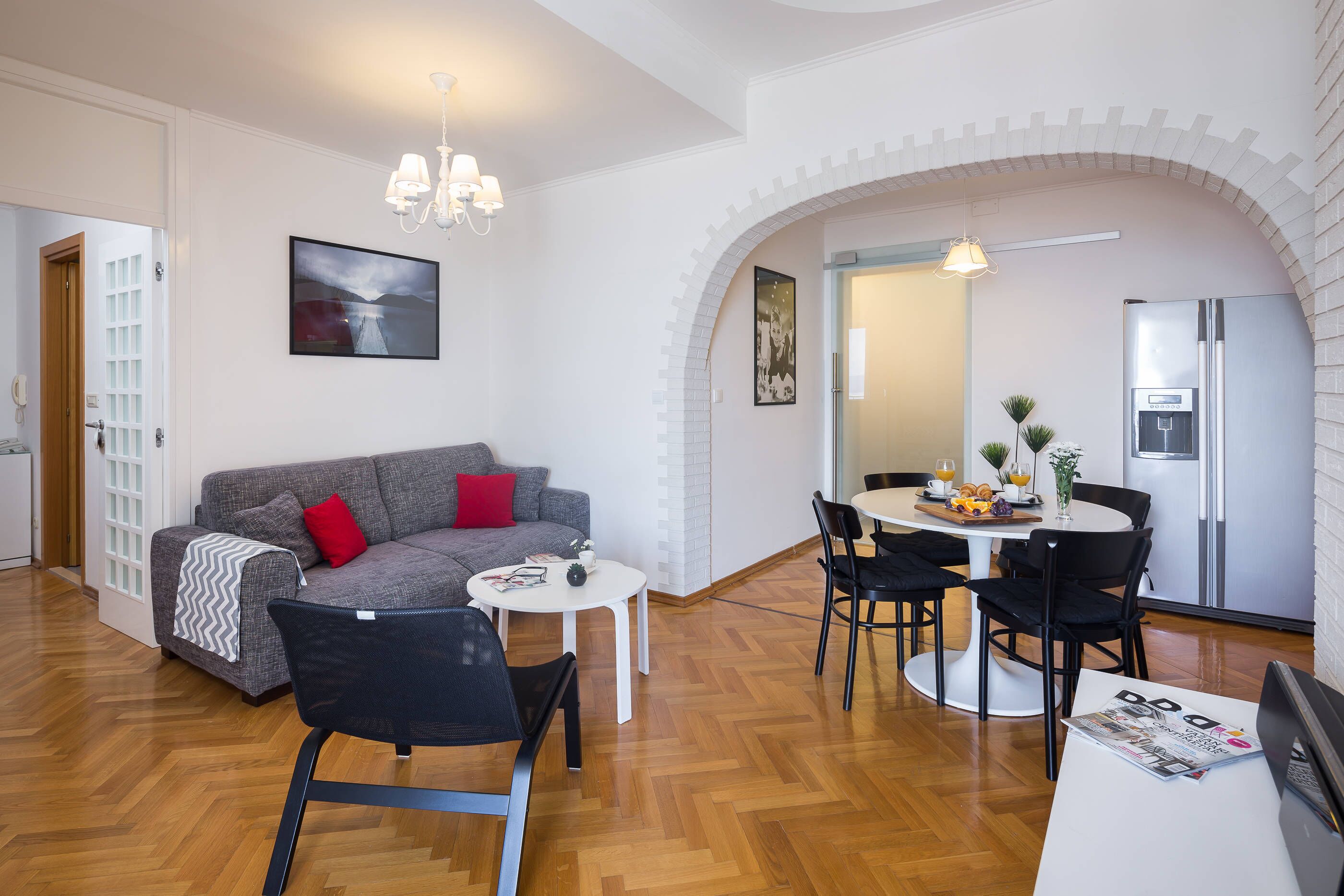 A modern living room with a sofa, dining table, chairs, and a kitchen area with a refrigerator.