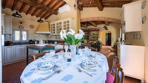 A dining area with a round table set for a meal, surrounded by kitchen cabinets and a living area with a fireplace.