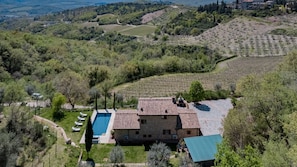 A stone villa with a swimming pool, surrounded by vineyards and lush greenery.