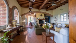 A spacious living area with a fireplace, a dining area, and a kitchen. There is a large window providing natural light and a view of the outdoors. - Casa Perano, Gaiole in Chianti, Siena and Chianti (Gaiole in Chianti)