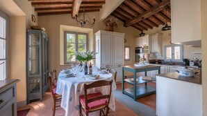 A dining area with a table set for four, a kitchen with modern appliances, and a rustic wooden ceiling. - Casa Perano, Gaiole in Chianti, Siena and Chianti (Gaiole in Chianti)