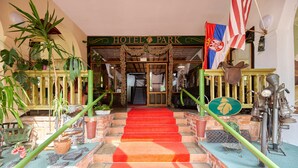 A hotel entrance with a red carpet, a sign reading "HOTEL PARK," and various plants and artifacts on either side of the stairs. - Park Inn Resort (Miroslawiec)