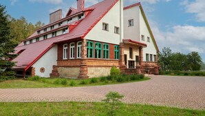 A two-story house with a red roof and white walls, surrounded by a paved driveway and greenery. - Park Inn Resort (Miroslawiec)