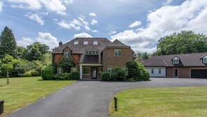 A two-story house with a paved driveway leading to the entrance, surrounded by well-maintained lawns and mature trees. - Luxury country retreat with extensive leisure facilities (Lane End)