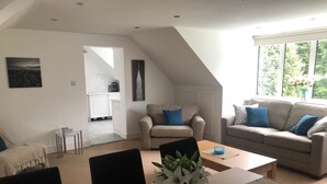 A modern living room with a dining area, a sofa, a coffee table, and a view of the outdoors through large windows. - Luxury country retreat with extensive leisure facilities (Lane End)