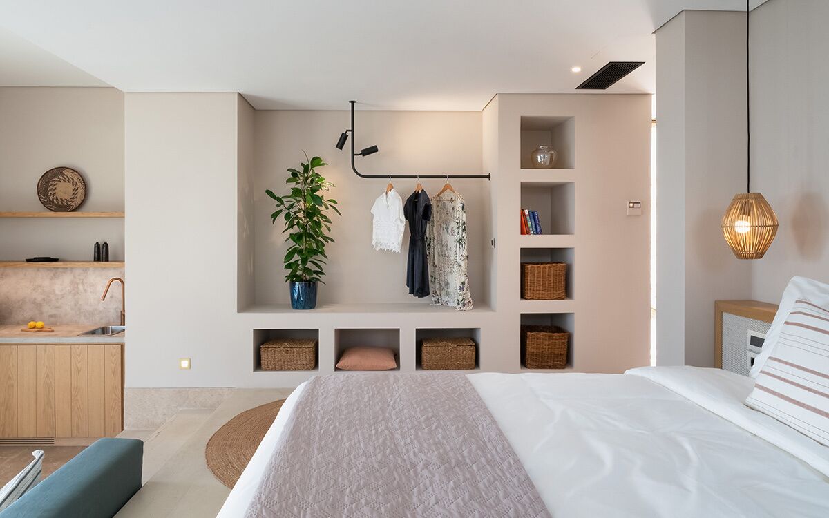 Un dormitorio moderno con una cama grande, una mesita de noche, una lámpara colgante y estanterías empotradas con cestas y una planta en maceta.