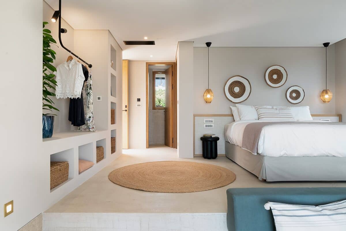Un dormitorio moderno con una cama grande, una mesita de noche, una alfombra redonda y un armario con ropa colgada.