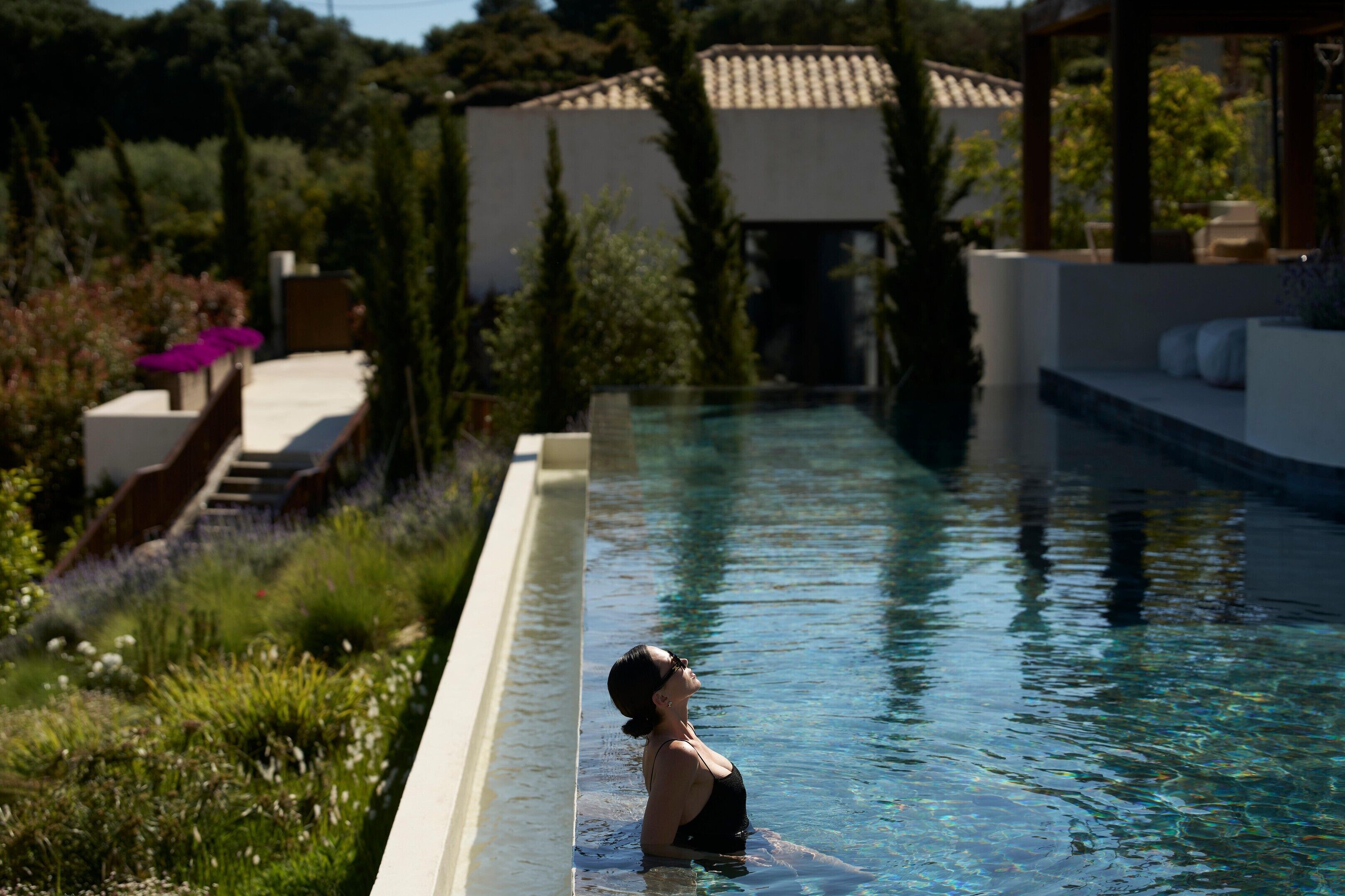 A swimming pool with a person in it, surrounded by greenery and a building in the background.