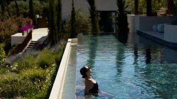 A swimming pool with a person in it, surrounded by greenery and a building in the background.