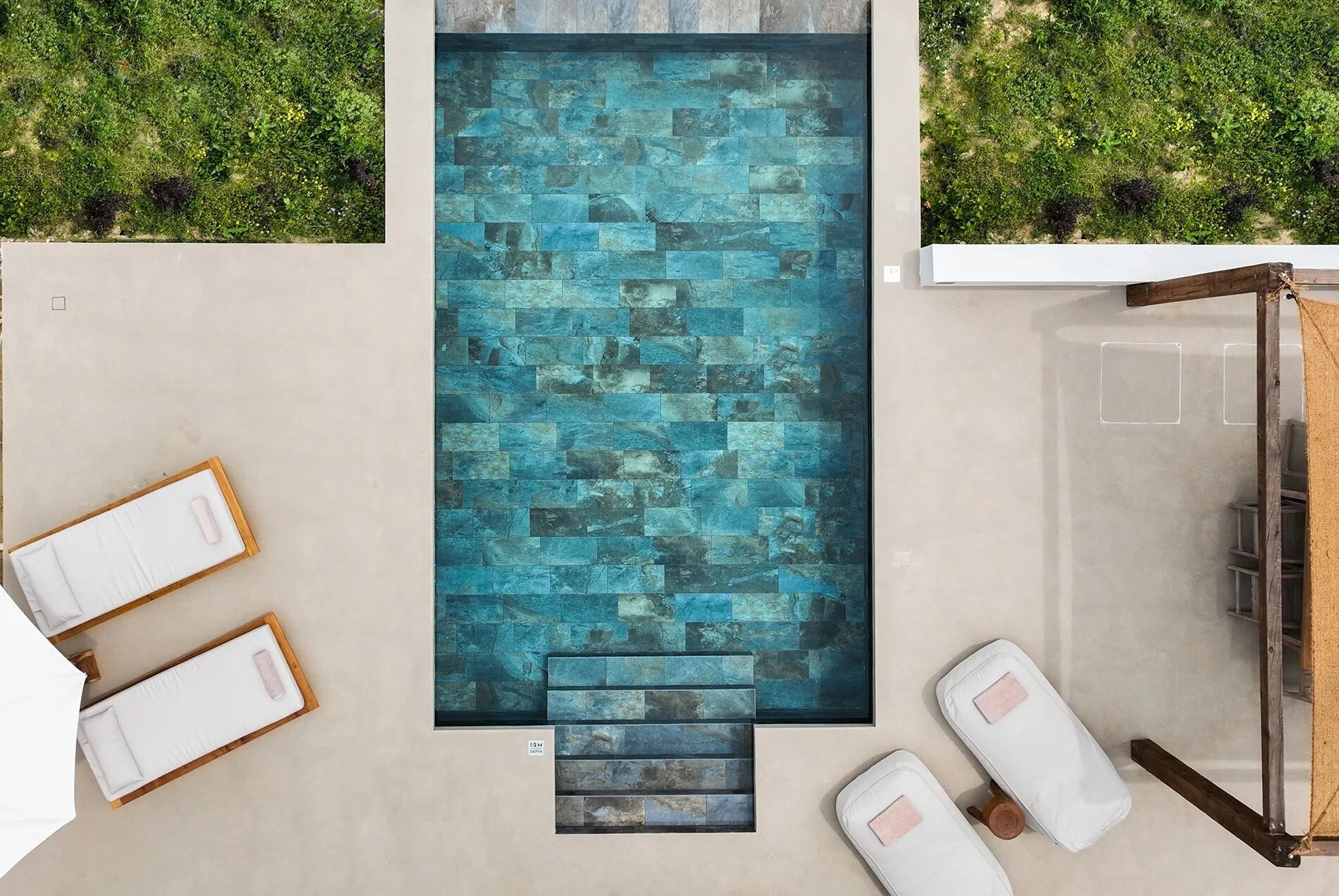 A rectangular pool with a blue mosaic tile design, surrounded by a light-colored deck.