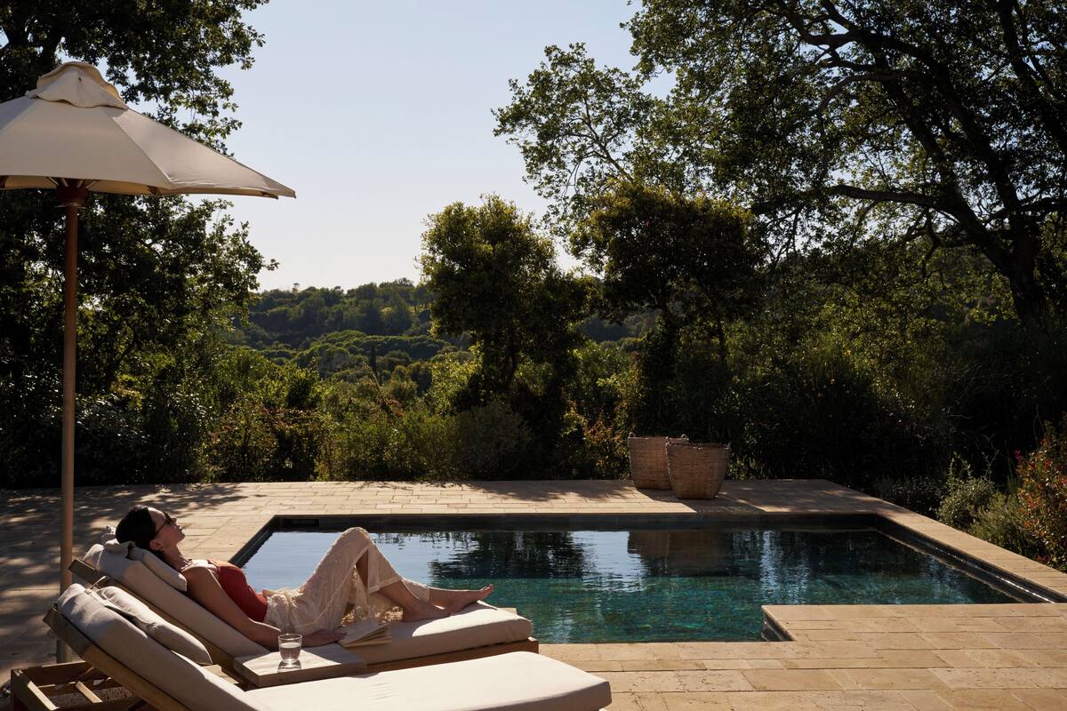 Zona de piscina con una silla de descanso, un vaso de agua y una sombrilla grande.