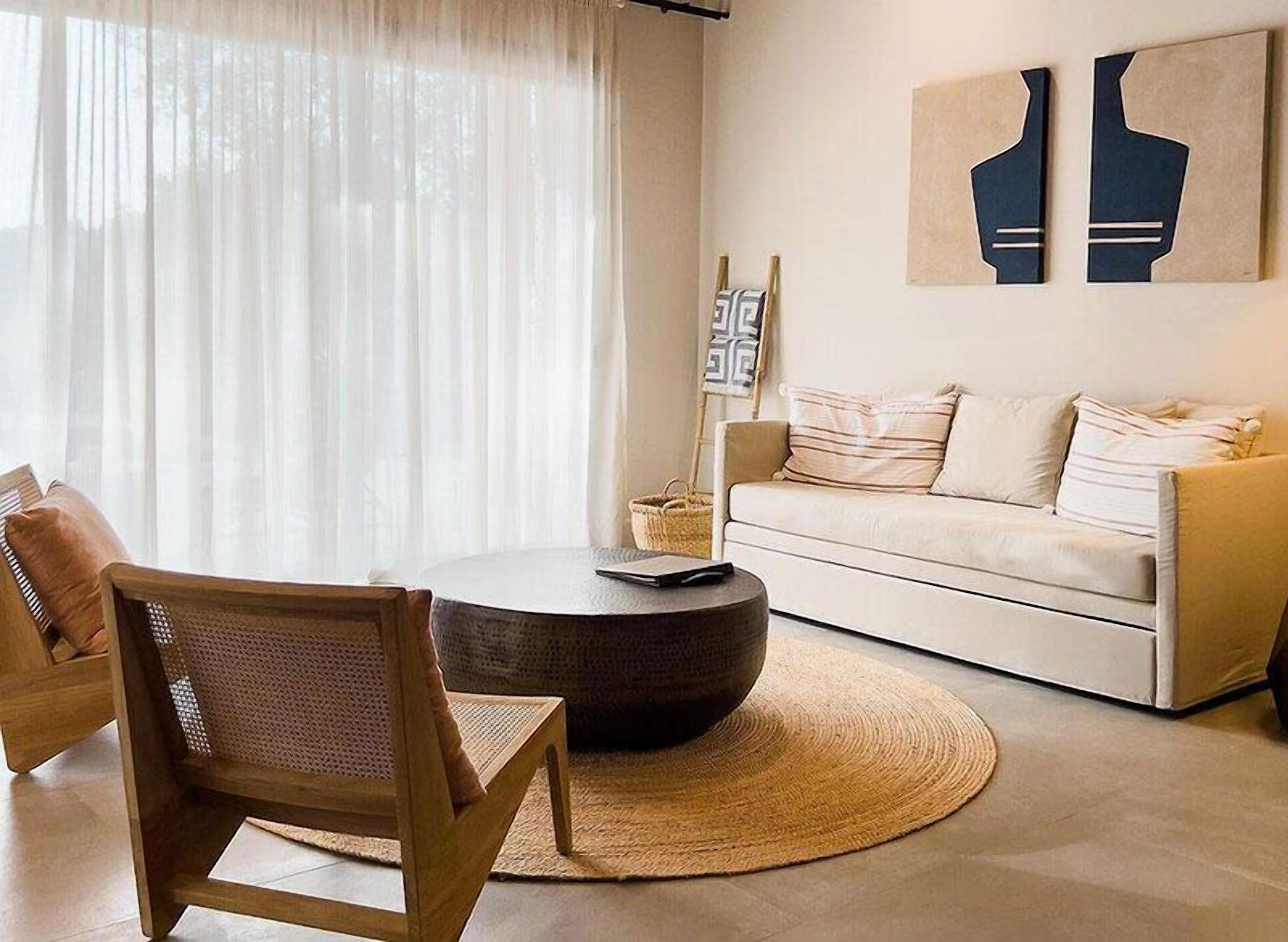 A modern living room with a round coffee table, a sofa, and a chair. There are abstract wall art pieces above the sofa.