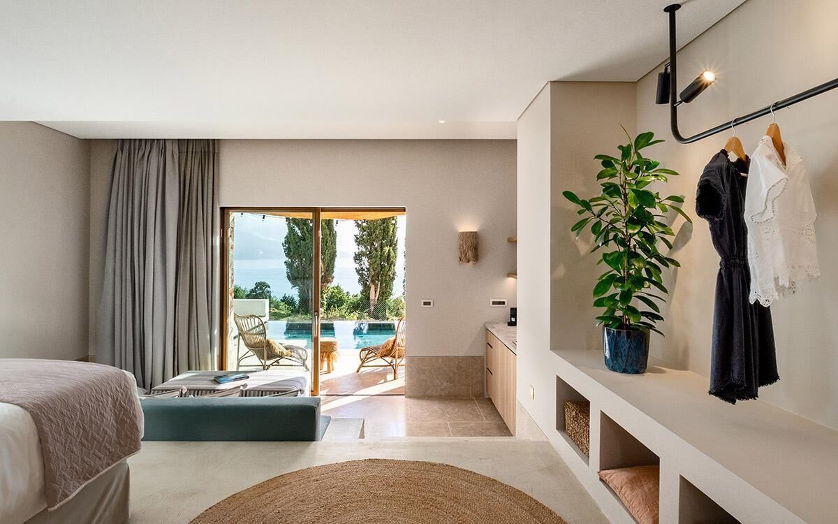 Ein modernes Hotelzimmer mit Bett, Sitzgelegenheit mit Blick auf einen Pool, einer kleinen Küchenzeile und einer Pflanze.