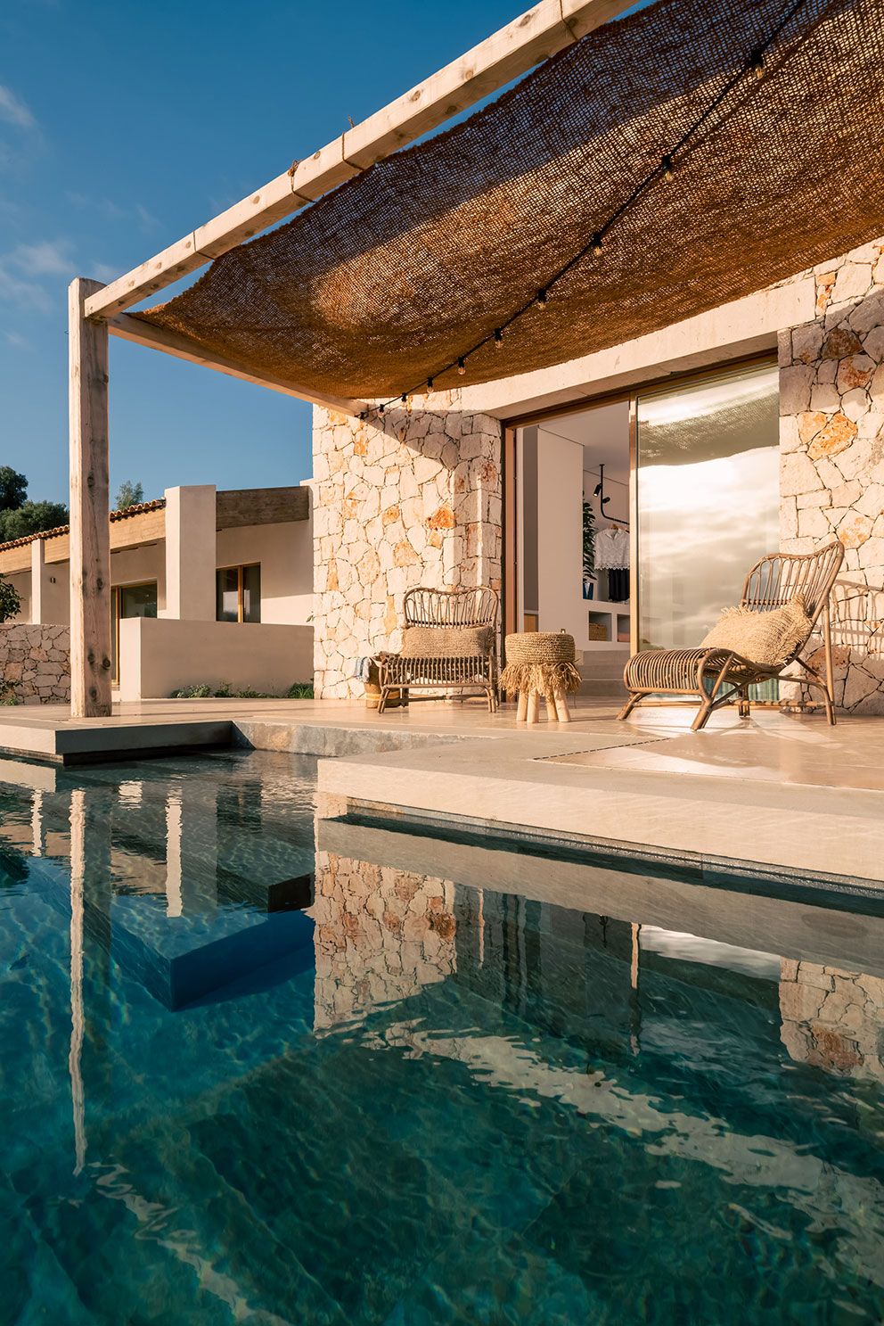 A modern house with a stone exterior, a swimming pool, and outdoor seating.