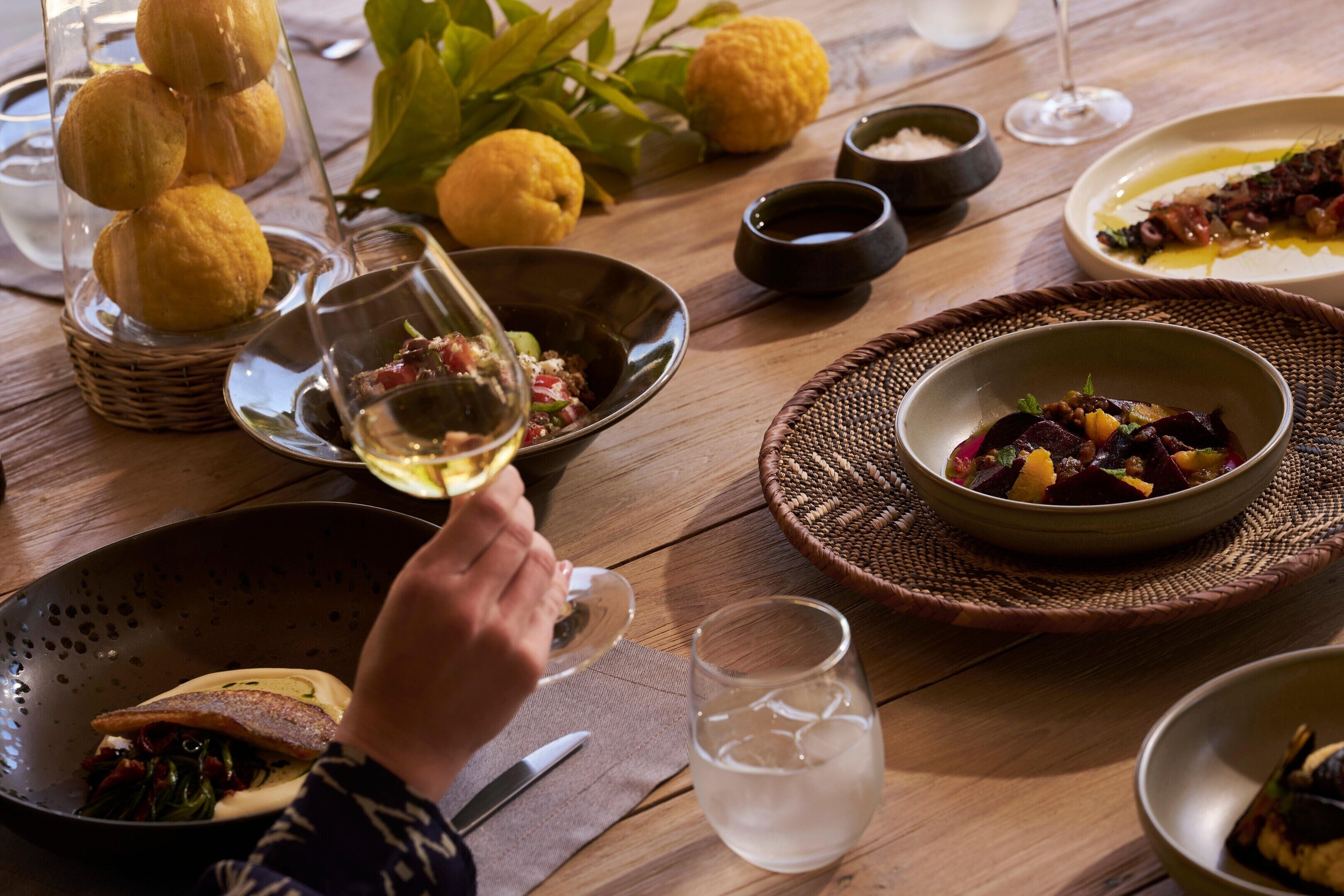 A dining table with various dishes, a glass of white wine, and a woven placemat.
