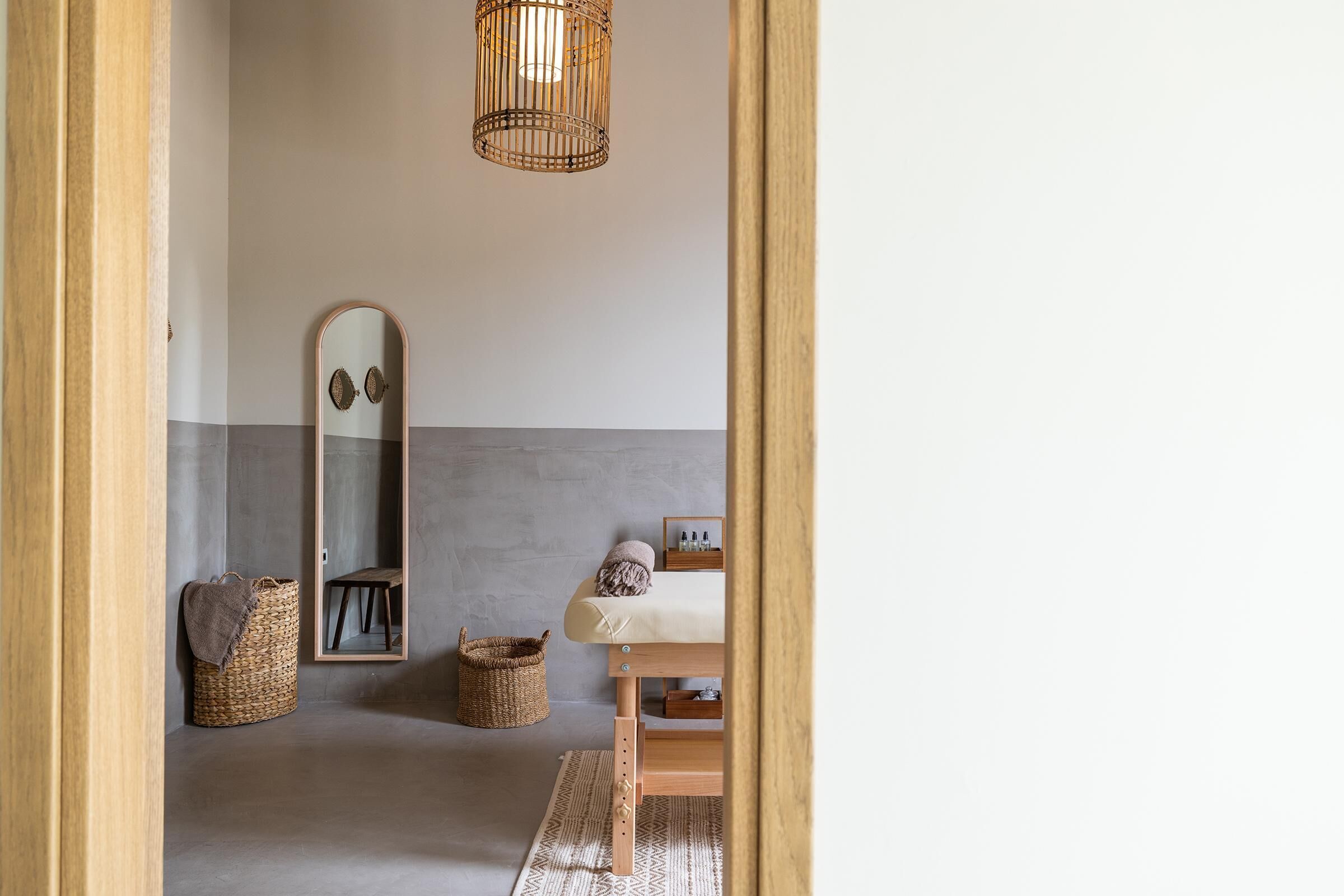 Un dormitorio minimalista con una cama de madera, un espejo grande, una lámpara colgante y una cesta tejida.