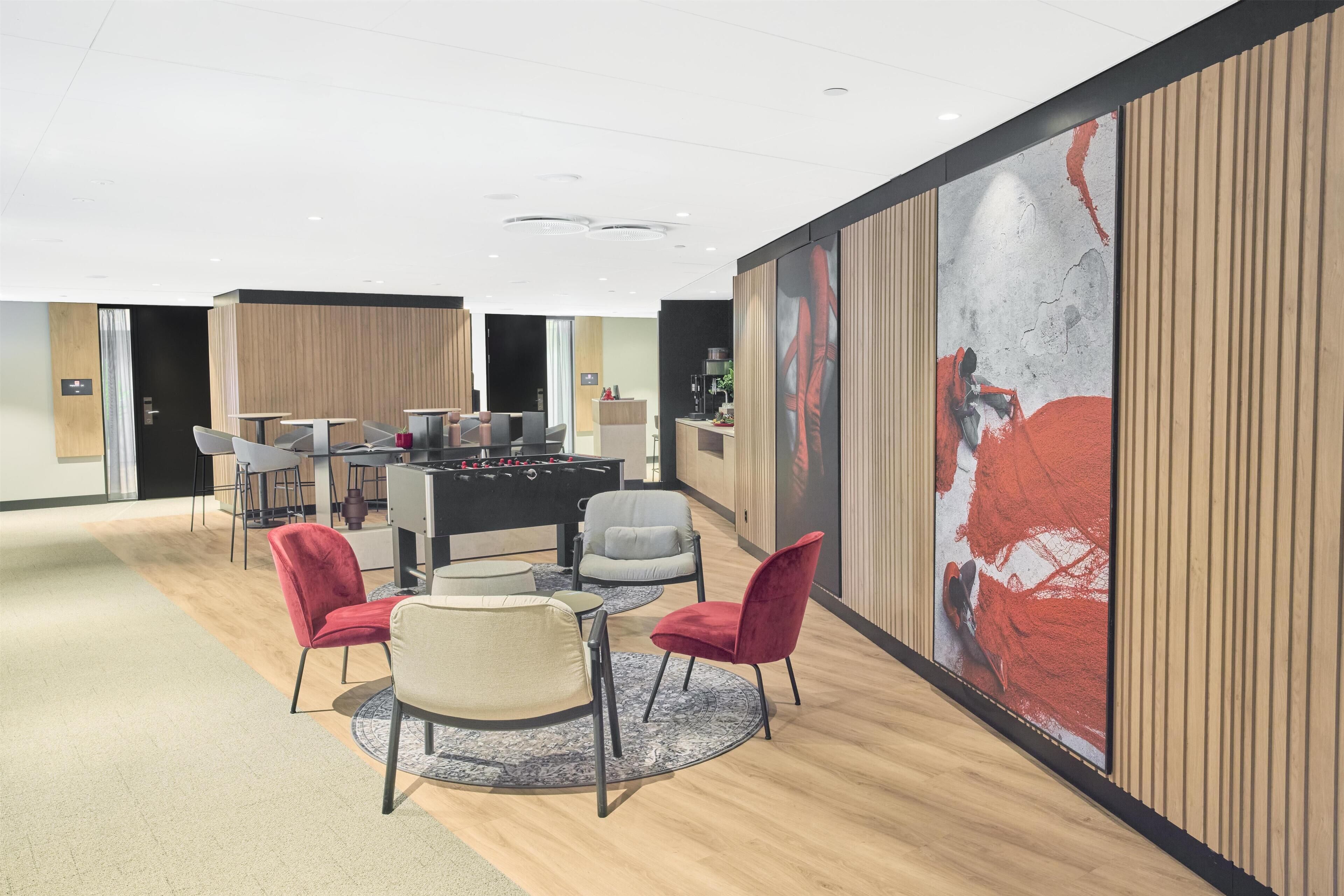 A modern lounge area with a foosball table, seating, and a large abstract painting on the wall.