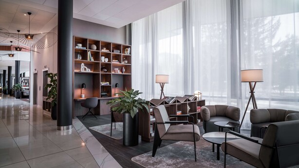 A modern lobby with a reception desk, seating area, and a large bookshelf.