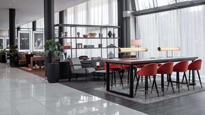 A modern interior with a dining area, red chairs, a black table, and a bookshelf with various decorative items. - Radisson RED Hotel, Oslo Airport (Ullensaker)