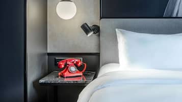 A hotel room with a bed, a nightstand with a red rotary phone, and a wall-mounted lamp.