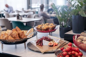 A buffet with croissants, grapes, cheese, and tomatoes.