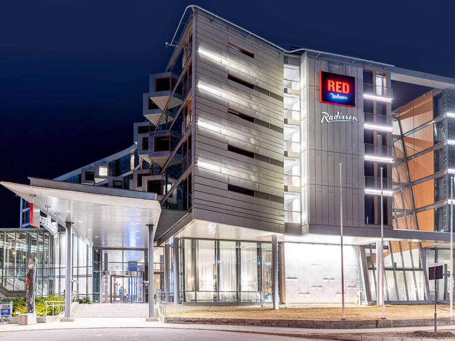 A modern hotel with a prominent 'RED Radisson' sign, a glass facade, and a unique architectural design with multiple levels and balconies.
