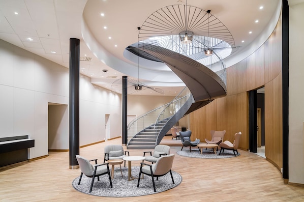 Un hall d’entrée spacieux, doté d’un escalier moderne, de coins salon confortables et d’un plafond haut orné de luminaires originaux.