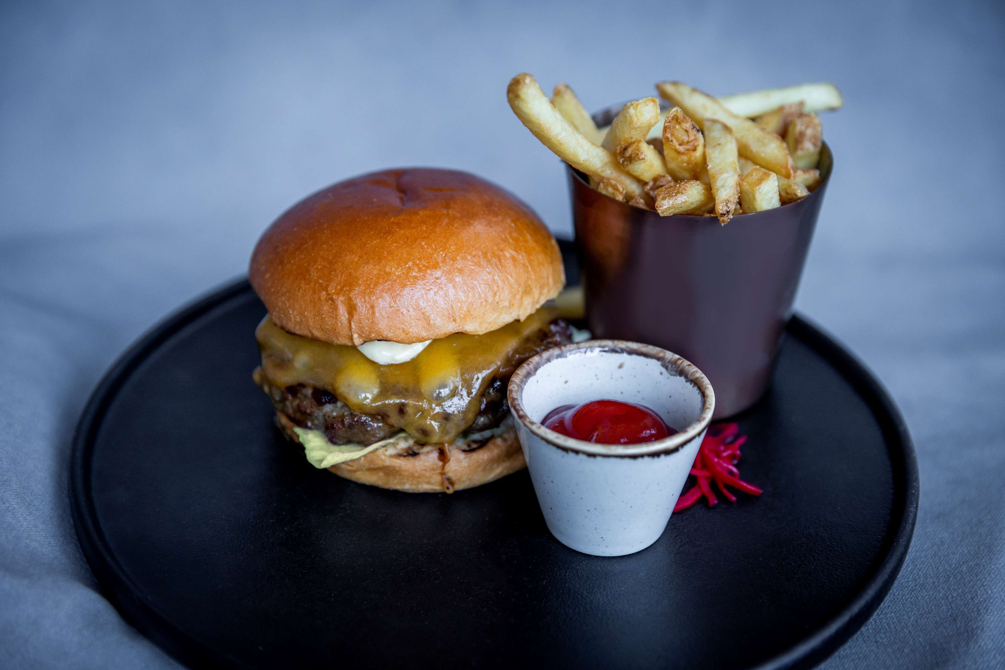 A burger with fries and ketchup on a black plate.