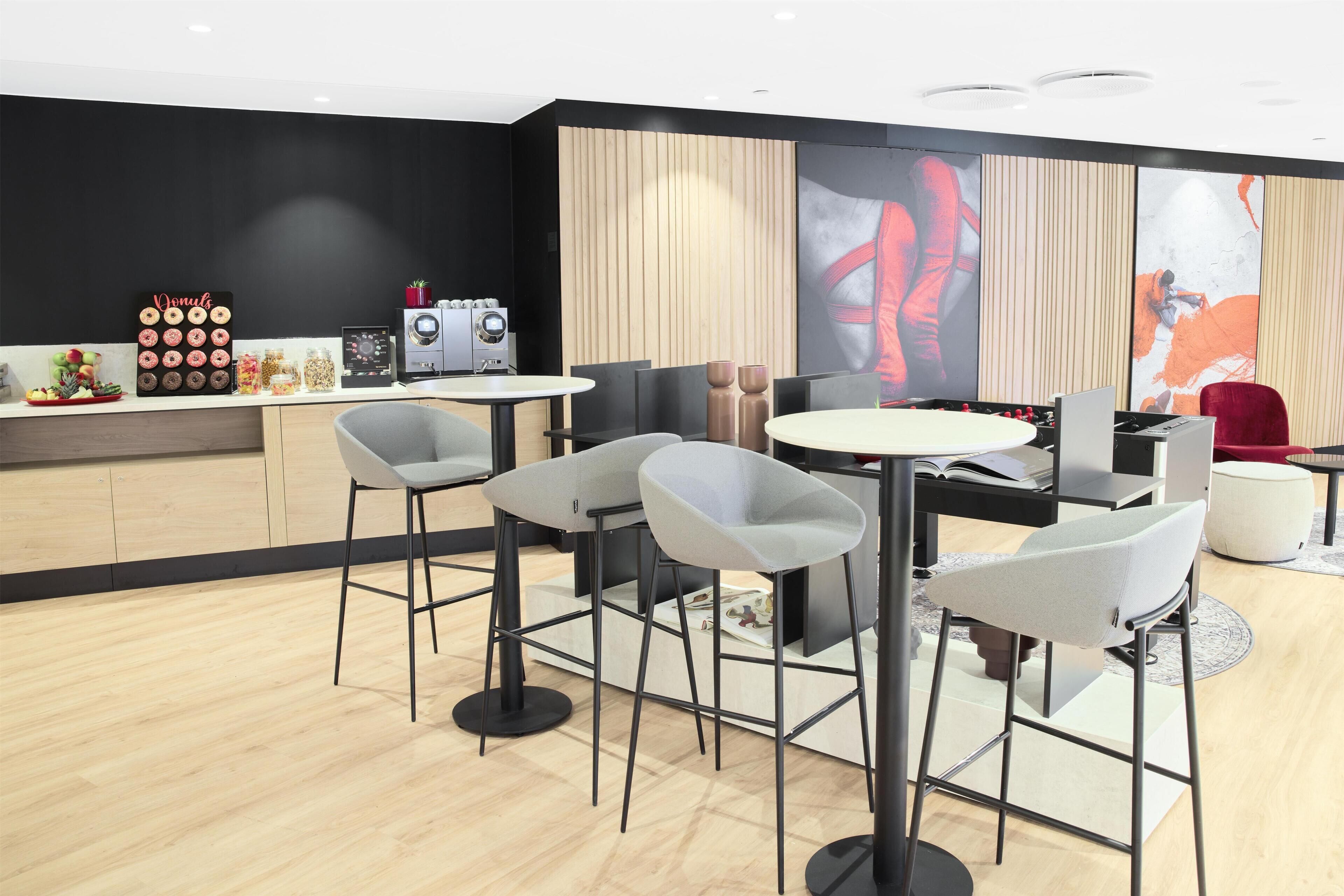 A modern dining area with bar stools, a round table, and a kitchen area with a coffee machine and jars of snacks.